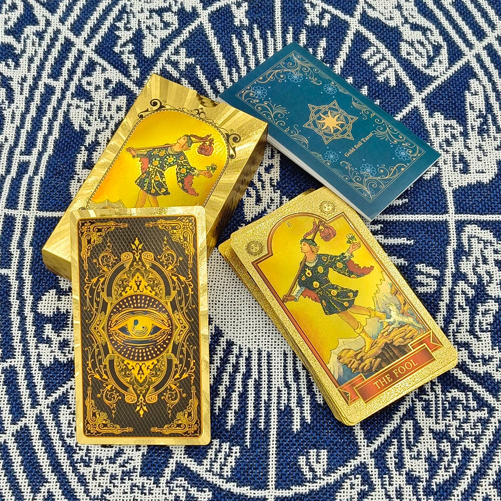 A set of gold foil tarot cards and a guidebook are displayed on a blue patterned fabric.