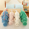 A collection of four soft stuffed dragon plush pillows in blue, pink, cream, and green resting on a bed.