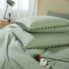 A light sage green duvet cover set with pom-pom trim resting on a bed.