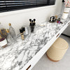 A white marble countertop displays various beauty tools and glass bottles under a window blind.