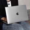 A person holds a silver laptop with a black Apple logo on it, resting on their lap.