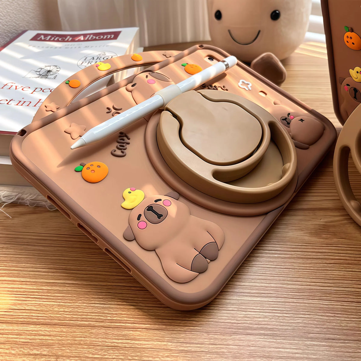 A silicone case featuring a cute cartoon capybara design for an iPad, shown on a wooden surface.