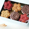 A tray of six floral-shaped cookies in shades of pink, peach, and brown on a white plate.