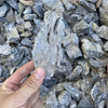 A hand holds a natural grey aquarium stone amidst a pile of similar stones for aquascaping.