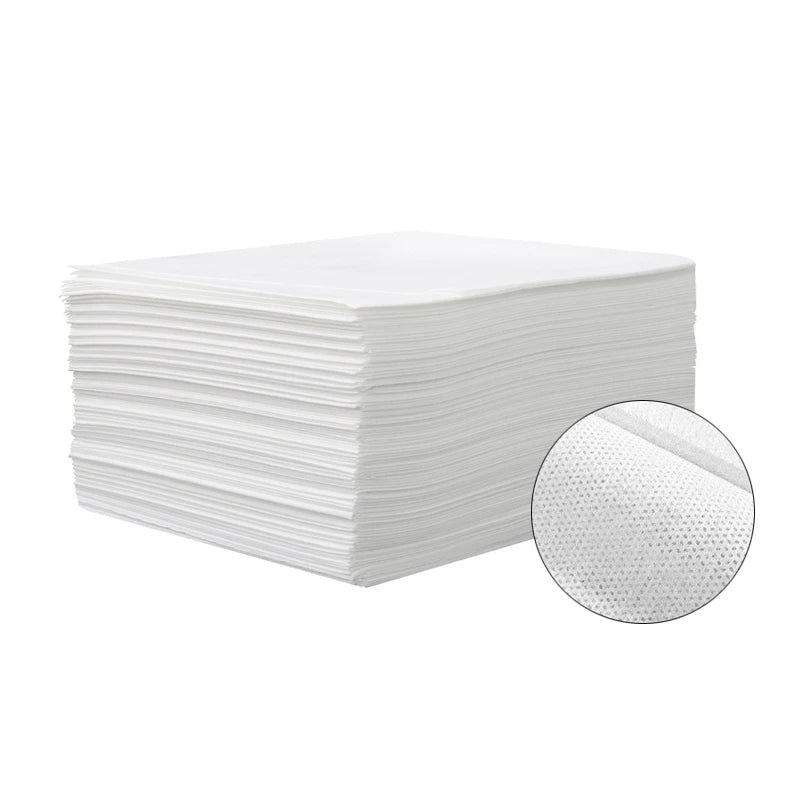 A stack of white premium disposable bed sheets for salons, spas, and travel, with a close-up view of the fabric texture.