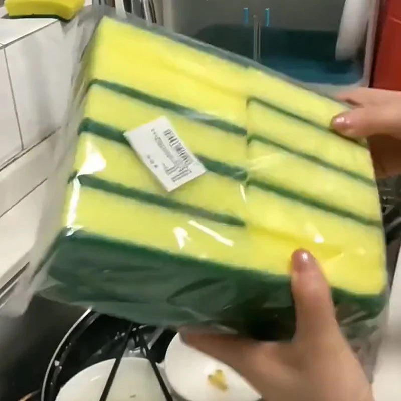 A clear plastic package of bright yellow and green double-sided kitchen scouring pads is being held by a hand.
