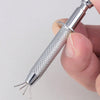 A hand holds a stainless steel piercing ball grabber tool with a textured handle and multiple prongs.