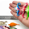 A hand holds a set of ten mini dinosaur figurines, including a blue dragon, pink tyrannosaurus, and various green and purple 