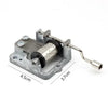 A vintage hand-crank music box mechanism with a silver metal frame and wooden cylinder.