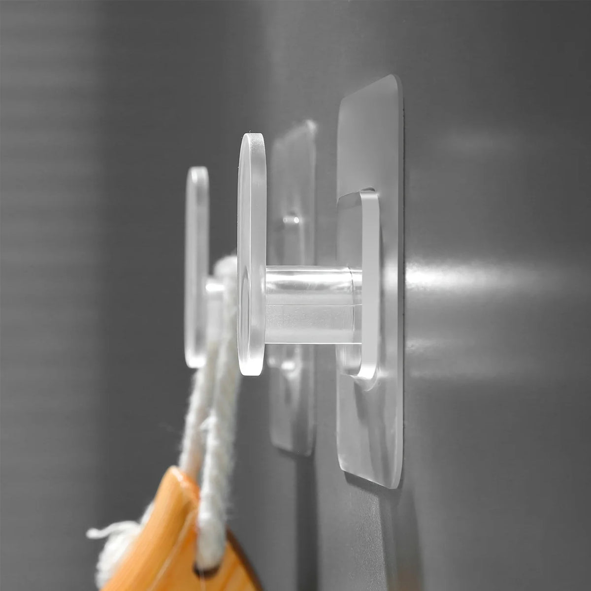 A close-up of a clear, extra-large adhesive hook mounted on a gray surface, with a white cord attached.