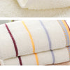 A stack of white bath towels with stripes in shades of yellow, purple, and gray.