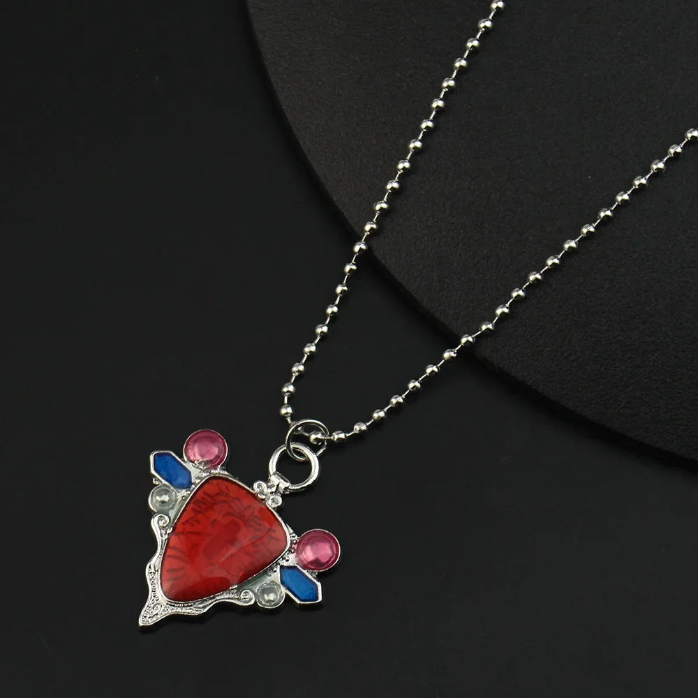 A silver pendant necklace featuring a red stone and blue accents, set against a black background.