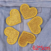 A set of five gold glitter heart patches sewn onto a denim fabric.