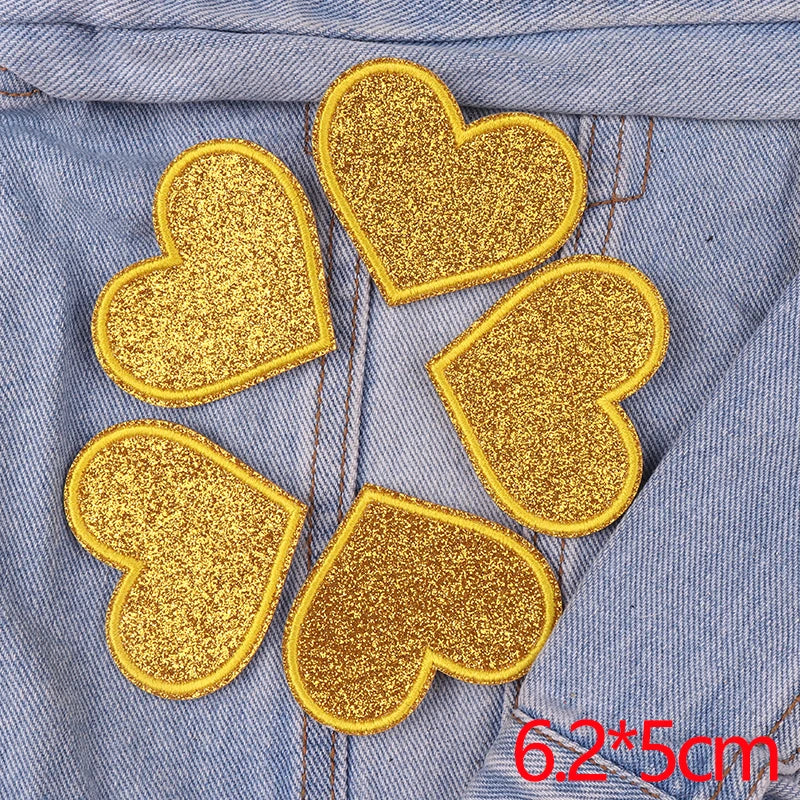 A set of five gold glitter heart patches sewn onto a denim fabric.