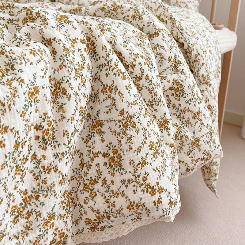 A close-up of a cream and gold floral muslin baby blanket draped on a wooden surface.