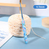 A blue ergonomic crochet hook with a bee design is shown next to a ball of light-colored yarn.
