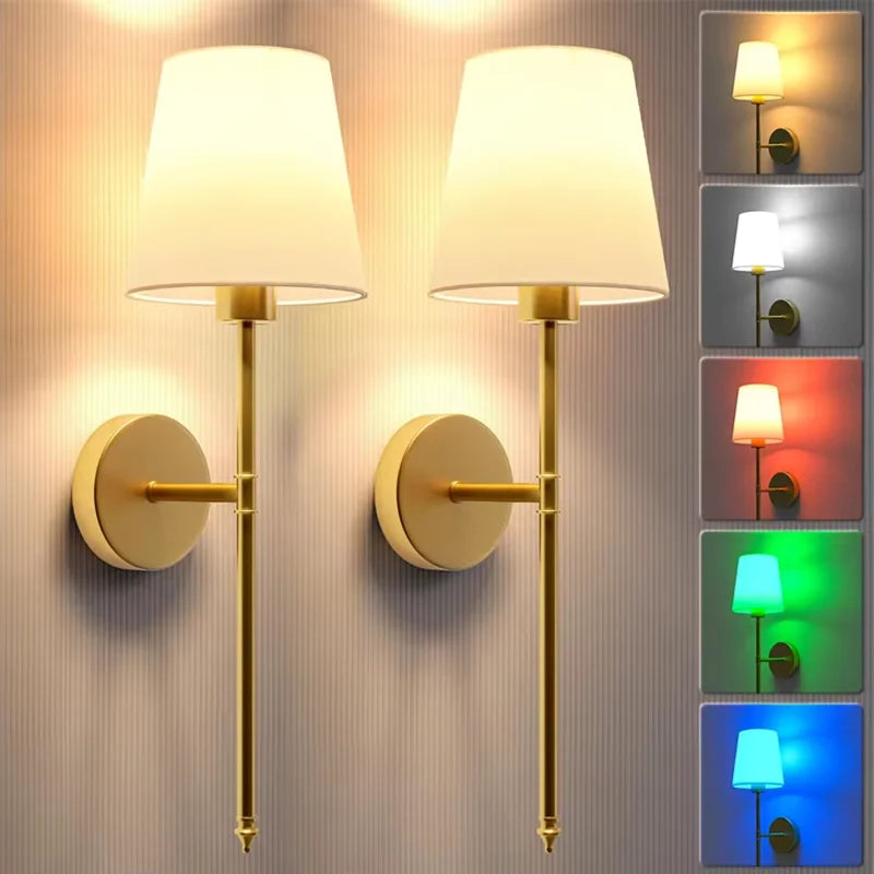 A set of modern brass wall lamps with white shades and colored light options mounted on a textured wall.