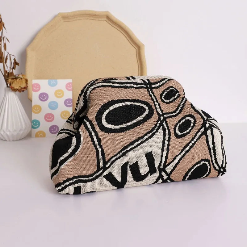 A hand-knit clutch bag featuring a beige and black geometric pattern with pearl accents, resting in front of a light yellow b