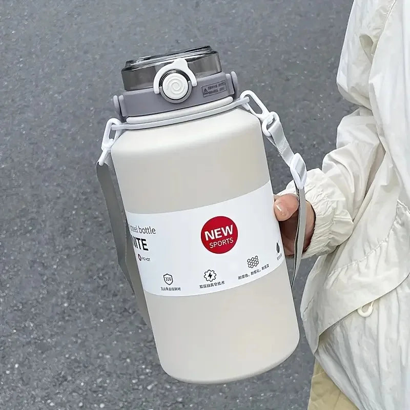 A white insulated stainless steel tumbler with a silver lid and handle is held by a person against a gray background.