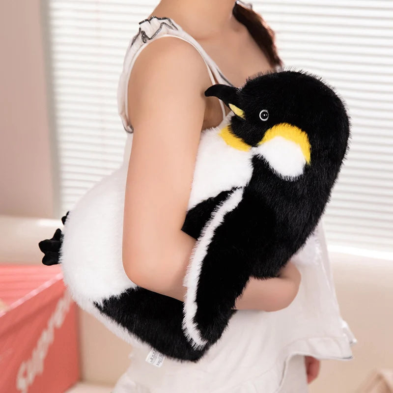 A person is holding a black and white penguin plush toy with yellow accents.