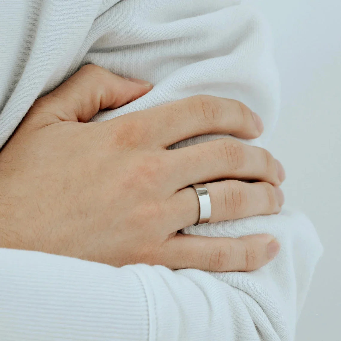 A close-up of a hand wearing a silver band ring, held by a person in a white sweater.
