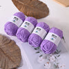 Purple Milk Cotton yarn skeins resting on a white surface next to dried leaves.