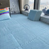 Light blue interlocking foam floor tiles with a colorful pillow and a gray plush toy near a window view