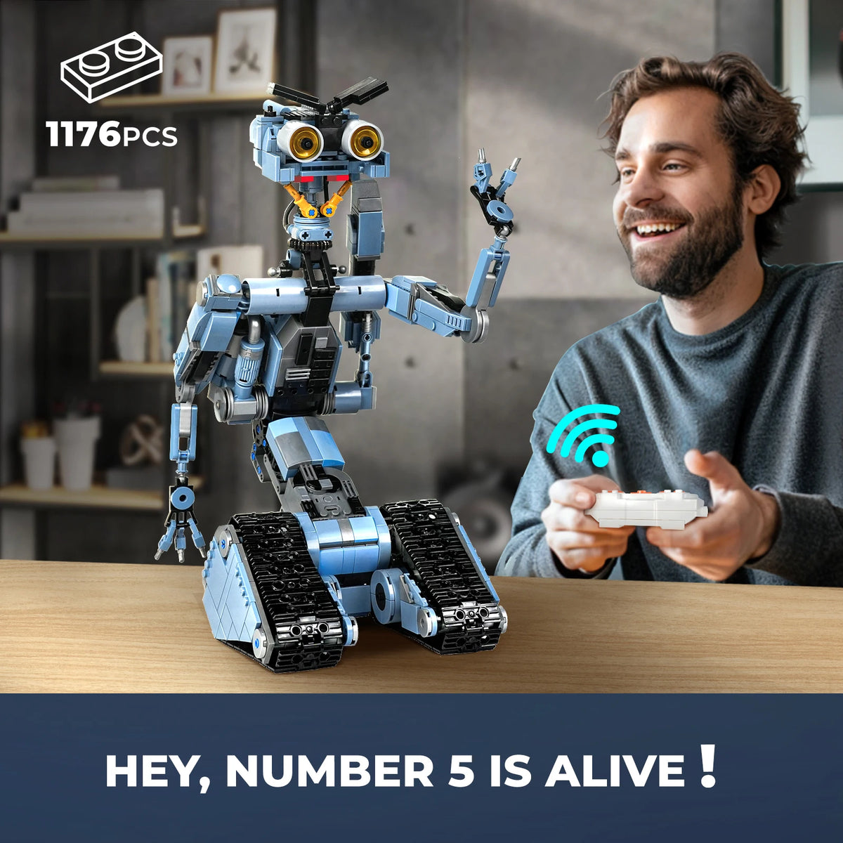 A man is holding a small white object while a blue and silver robot model sits on a wooden table.