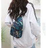 A person wearing a light gray sweatshirt is carrying a colorful leaf print sling crossbody bag on their back.