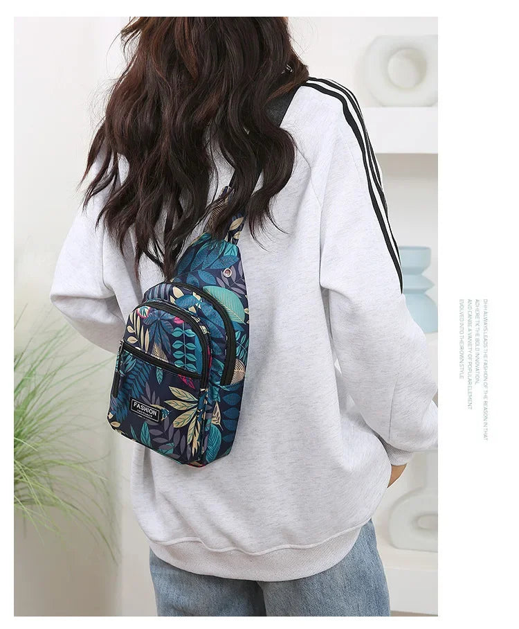 A person wearing a light gray sweatshirt is carrying a colorful leaf print sling crossbody bag on their back.