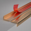 A close-up view of self-adhesive metal L-shaped corner protector strips in copper and red finishes.