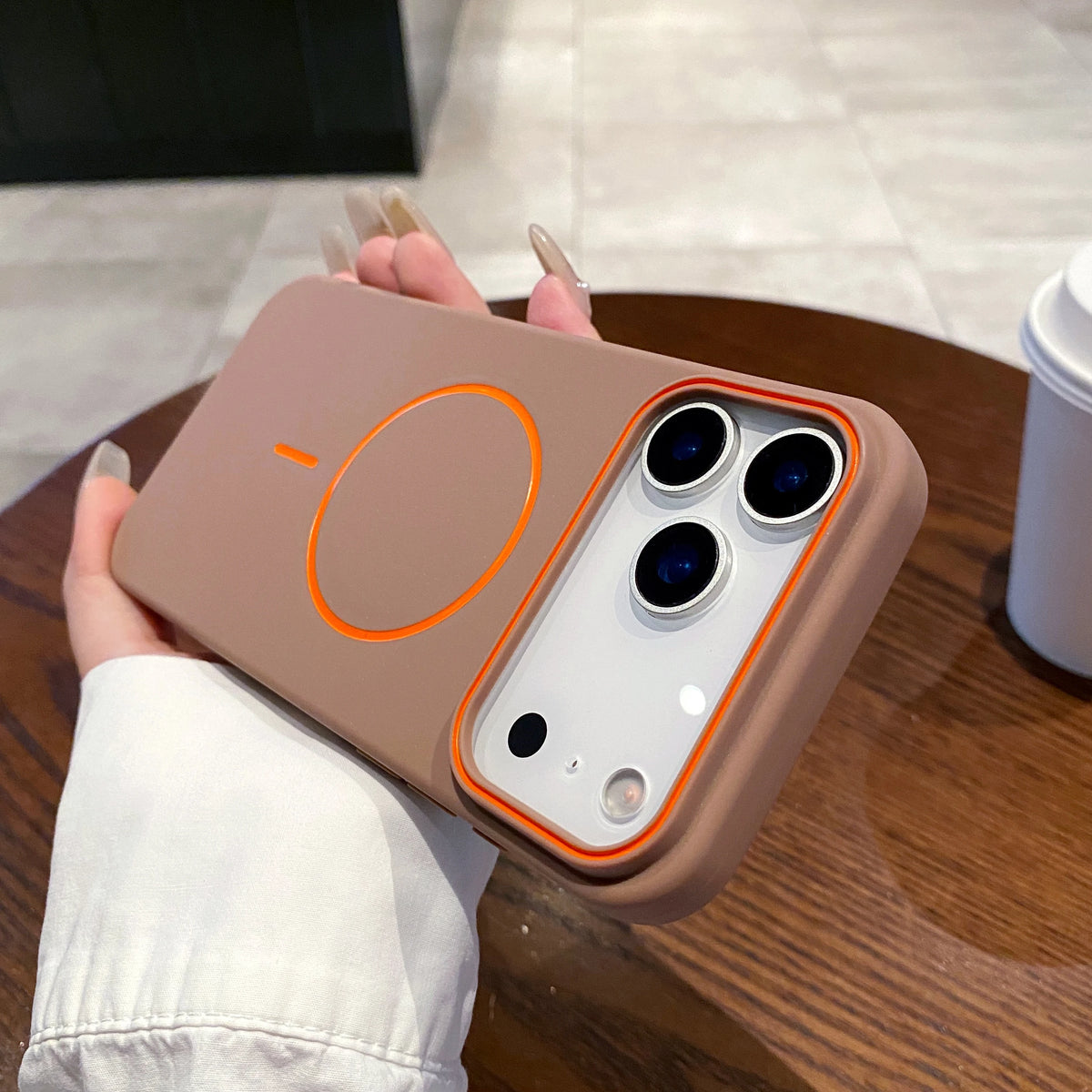 A hand holds a matte brown phone case with MagSafe support and three camera lenses.