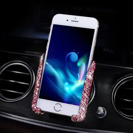 A white smartphone is held in a crystal air vent car phone holder on a black surface.