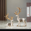 A set of two resin deer figurines with golden antlers and decorative patterns displayed on a marble surface.