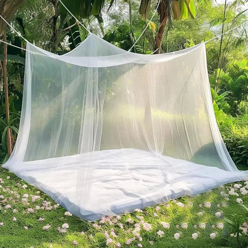 A sheer white lace canopy mosquito net draped over a bed in a lush green garden setting.