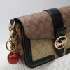 Braune Tasche mit schwarzem Zier und goldfarbenen Anhängern auf weißem Untergrund.