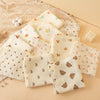 A collection of soft cotton gauze baby swaddle blankets in cream and beige tones arranged on a light background.