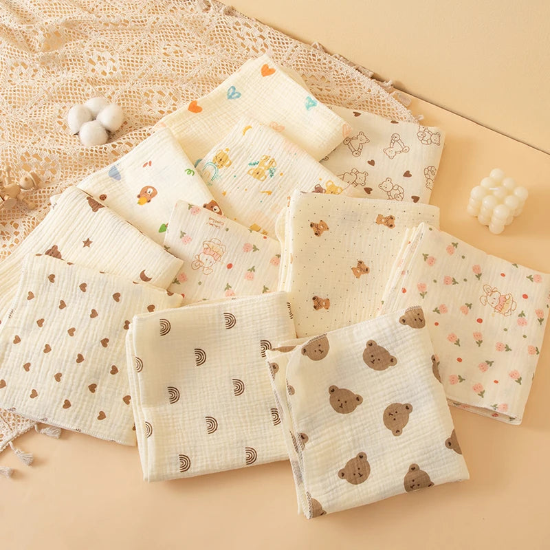 A collection of soft cotton gauze baby swaddle blankets in cream and beige tones arranged on a light background.