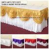 A long white table skirt with gold swag and ruffled fabric displayed on a maroon carpet.