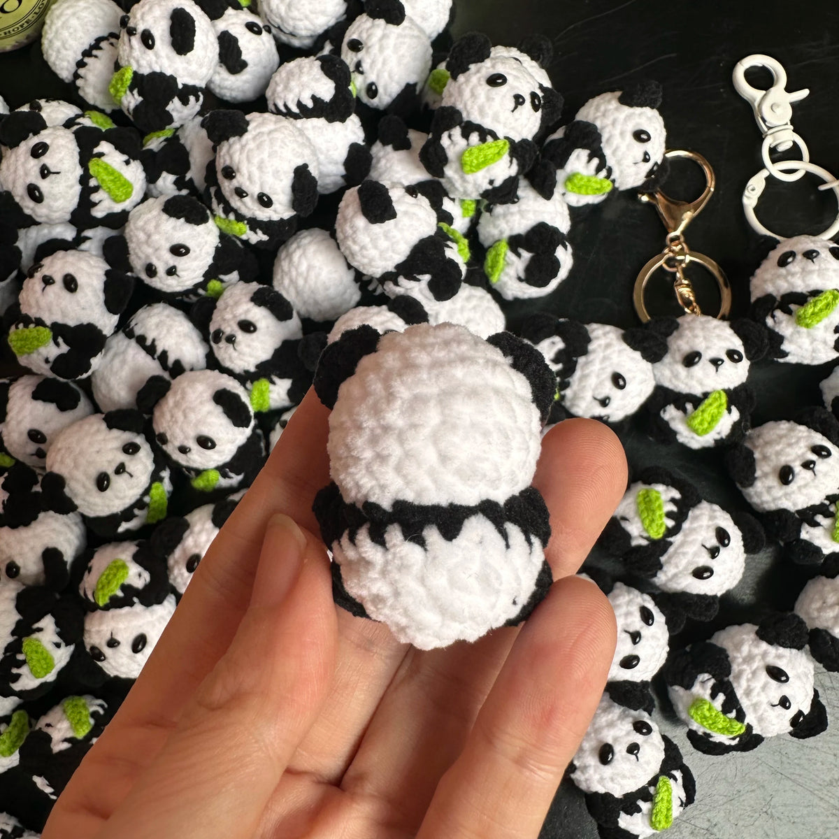 A hand holds a handmade crochet kitten keychain featuring a cute panda and cartoon animal charm.