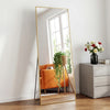 A full length mirror with a gold frame reflects an orange armchair and a window view.