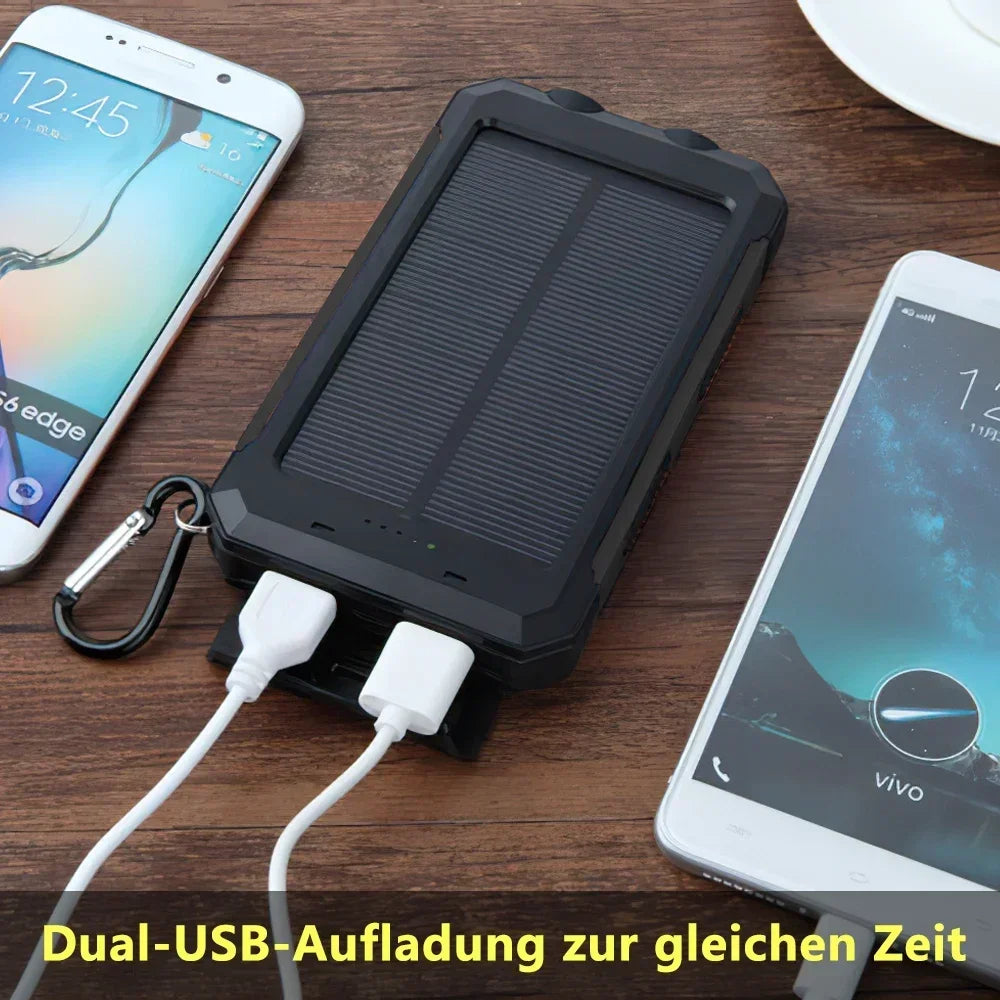 A black portable power bank is shown with a USB cable, next to a smartphone, demonstrating dual-USB charging.