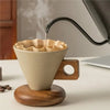 A ceramic coffee mug with a wood base is being filled by a steam wand, set against a light background.