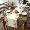 A table setting featuring a fall harvest table runner with orange pumpkins and autumn leaves on a wooden table.