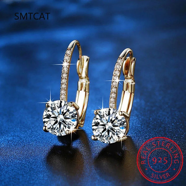 Pair of gold plated moissanite drop earrings displayed on a blue surface.