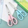 A pair of pink and light blue precision stainless steel scissors resting on a white lined paper next to a green ruler.
