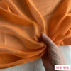 Close-up of flowing orange silk chiffon fabric being gathered by a hand.