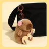 A brown capybara plush toy attached to a keyring, resting on a black fabric background.