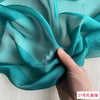 A close-up of teal silk chiffon fabric draped and folded, showing its sheer texture.