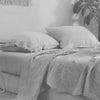 A close-up of a white linen bed sheet set with pillows on a bed.